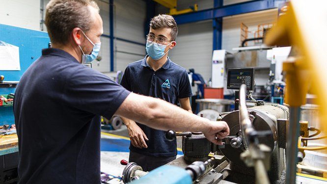 2 personnes(formateur/apprenti) se parlent devant une machine dans un atelier